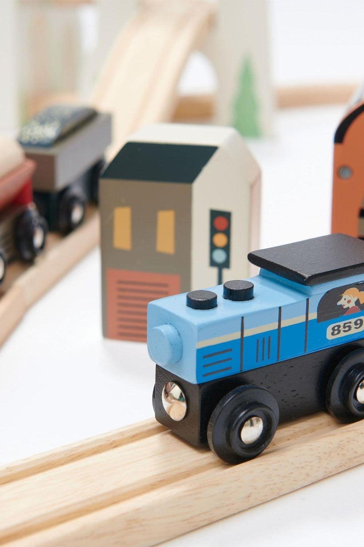 A colorful wooden train set features a blue locomotive and various building structures on a curved track, showcasing a playful, imaginative design perfect for young children.