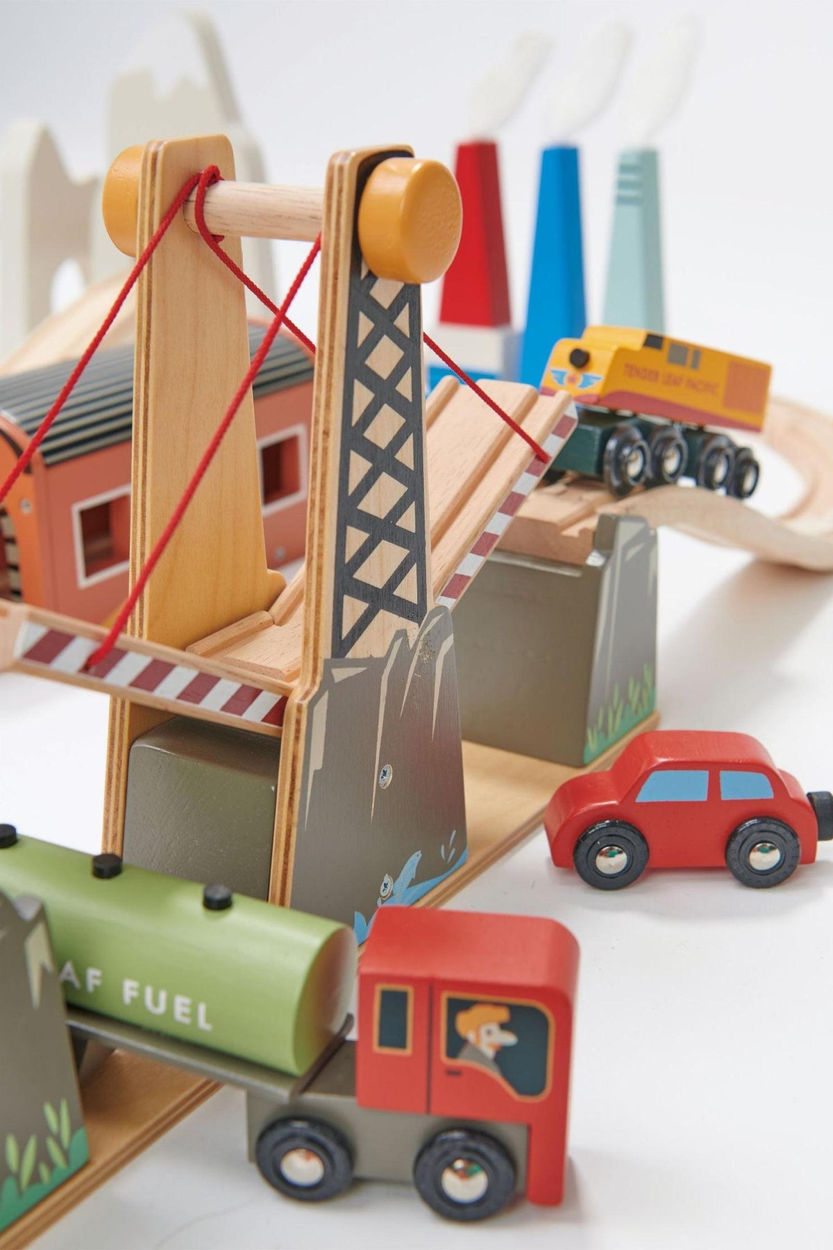 Colorful wooden train set featuring a lifting road bridge, factory buildings, and various vehicles, designed for imaginative play. Made by Tender Leaf Toys, it promotes sustainable, eco-friendly play for children.