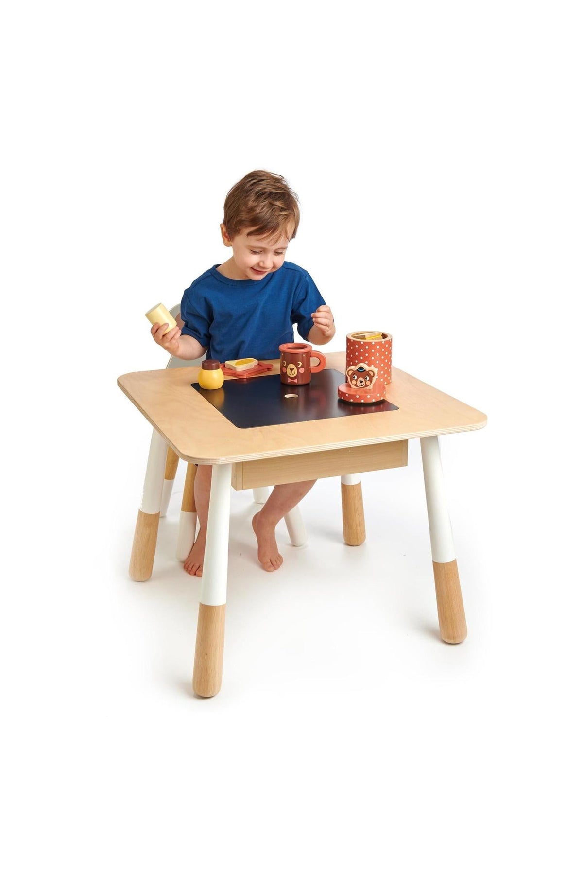 A child plays with toys on a light wooden table with white legs and a black chalkboard center.