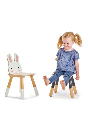 A young girl sits on a black and natural wood toddler chair, featuring a rabbit design on the backrest.