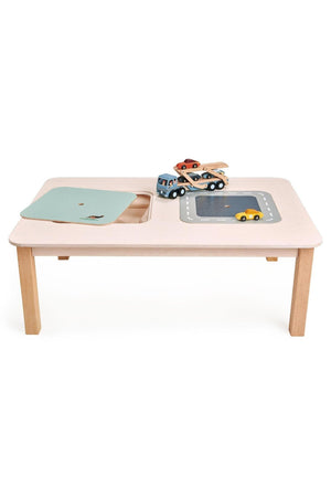 A spacious wooden play table in soft pink features two canvas storage compartments and reversible lids.