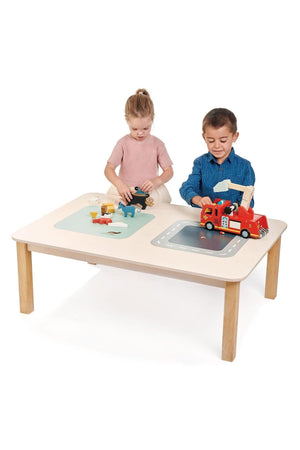 Two children play at a spacious, light-colored wooden table featuring a road and a nature-themed design. The table encourages imaginative play with various toys and vehicles.