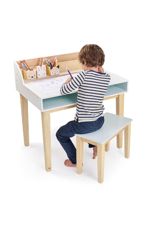 A child sits at a wooden desk, drawing with colored pencils. The sustainably built desk features a white surface and wooden legs, complemented by matching wooden pen pots.
