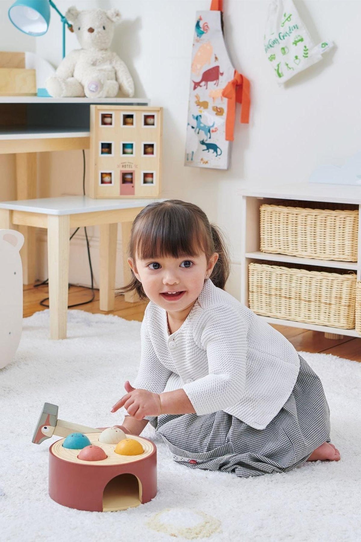 A young child plays with a colorful wooden hammer game on a soft rug in a bright, cozy room.