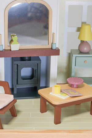 Wooden dollhouse interior with a fireplace, mirror, armchair, table, and lamp. Features eco-friendly materials and pastel colors.