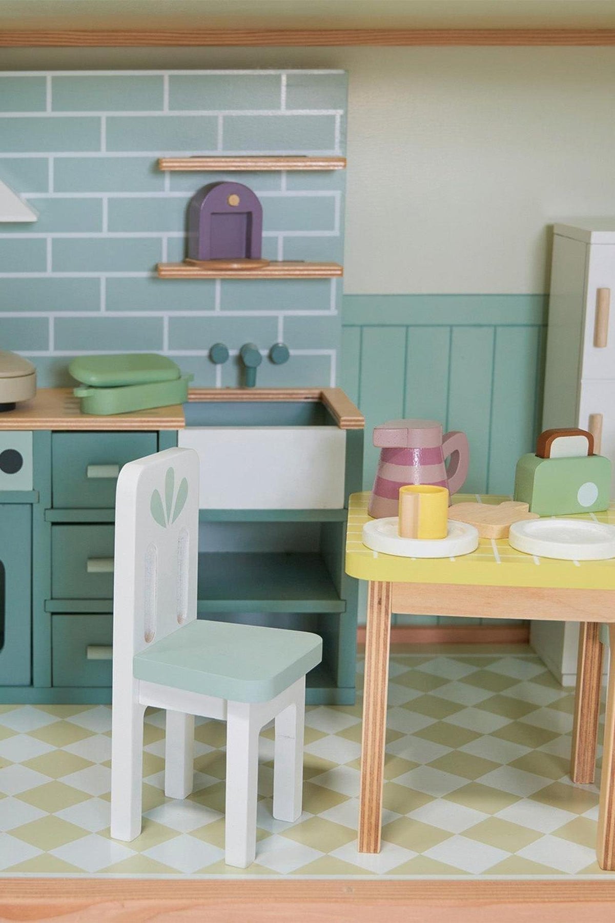 Wooden dollhouse kitchen with pastel colors, featuring a table, chairs, and kitchenware. Eco-friendly design with charming details.