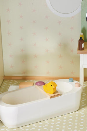 A wooden dollhouse bathroom with a white bathtub, yellow duck, and pastel accessories on patterned flooring.