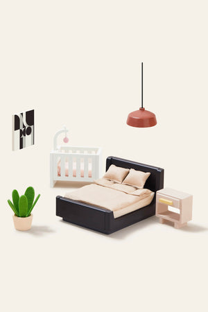 A stylish bedroom scene featuring a black bed with beige bedding, a white crib, a peach nightstand, a modern pendant light, and a potted cactus.