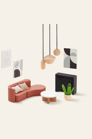 A modern dollhouse living room scene features a curved orange couch, a minimalist white coffee table, and a stylish black fireplace, complemented by abstract wall art and a potted plant.