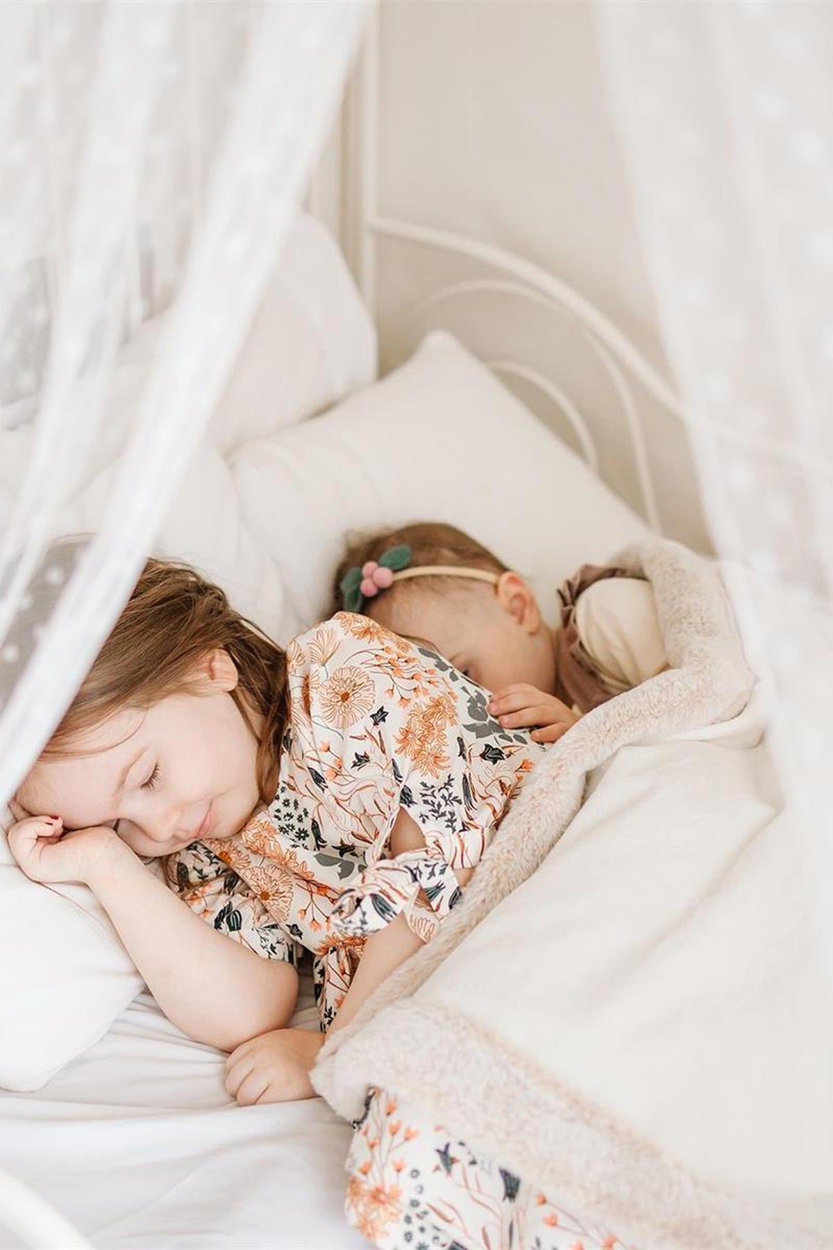 Two young girls peacefully sleeping in a cozy bed, surrounded by soft pillows and a fluffy blanket, with a delicate.