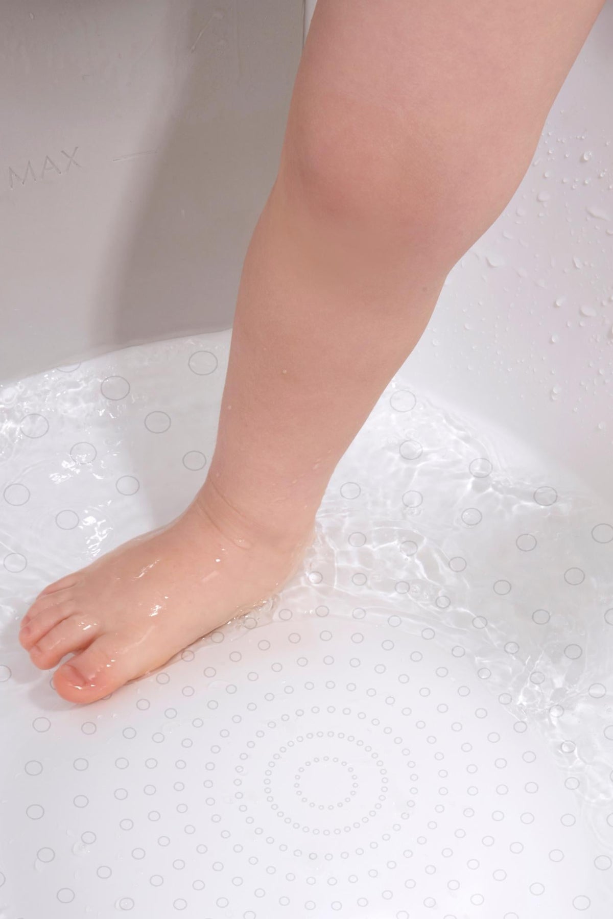 A childs foot is immersed in water inside a white bath with circular non-slip patterns.