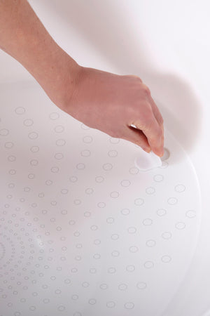 A hand removes a white plug from a bath tub with circular patterns on its surface.