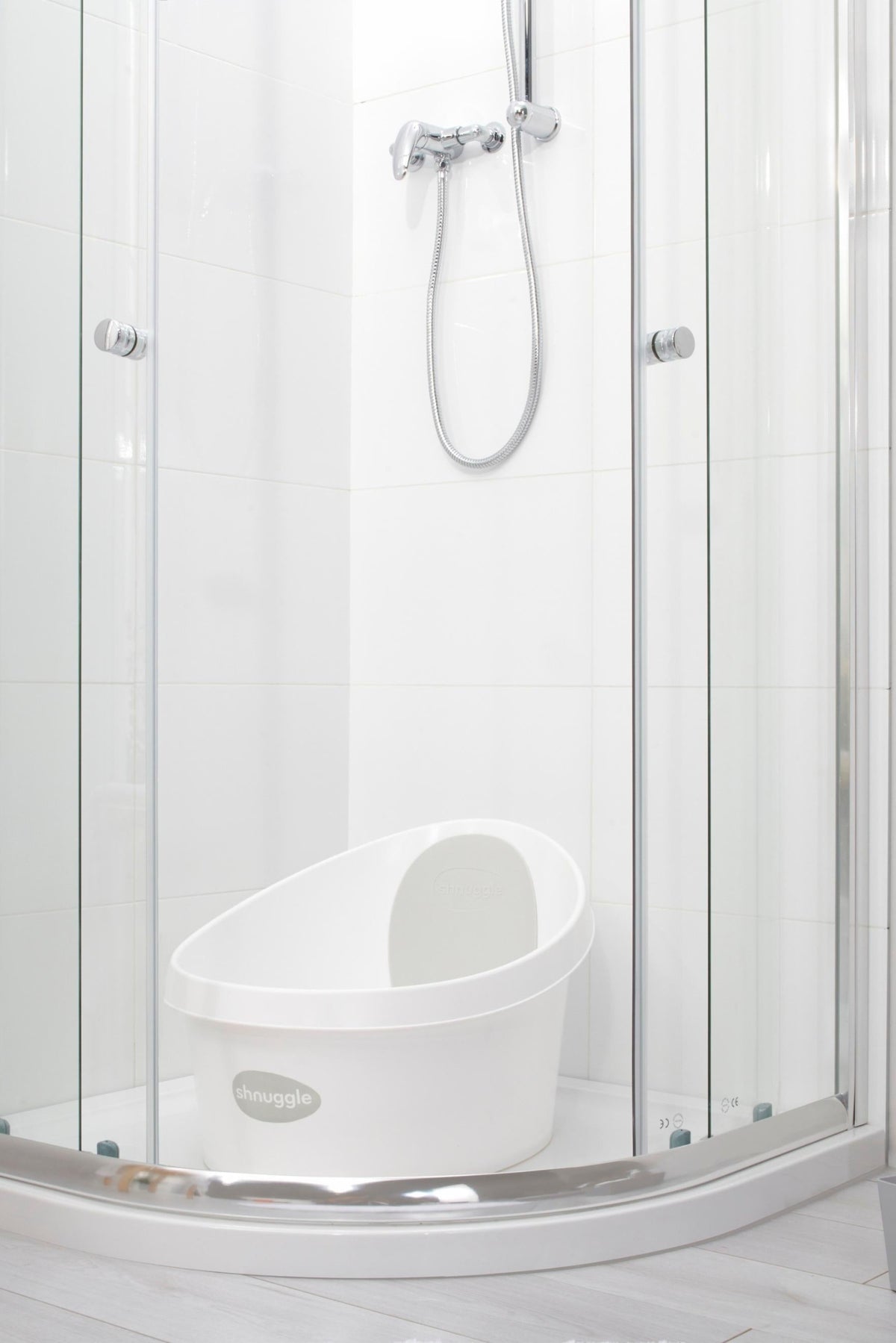 White Shnuggle Toddler Bath Tub in a modern shower enclosure with chrome fixtures and glass doors.