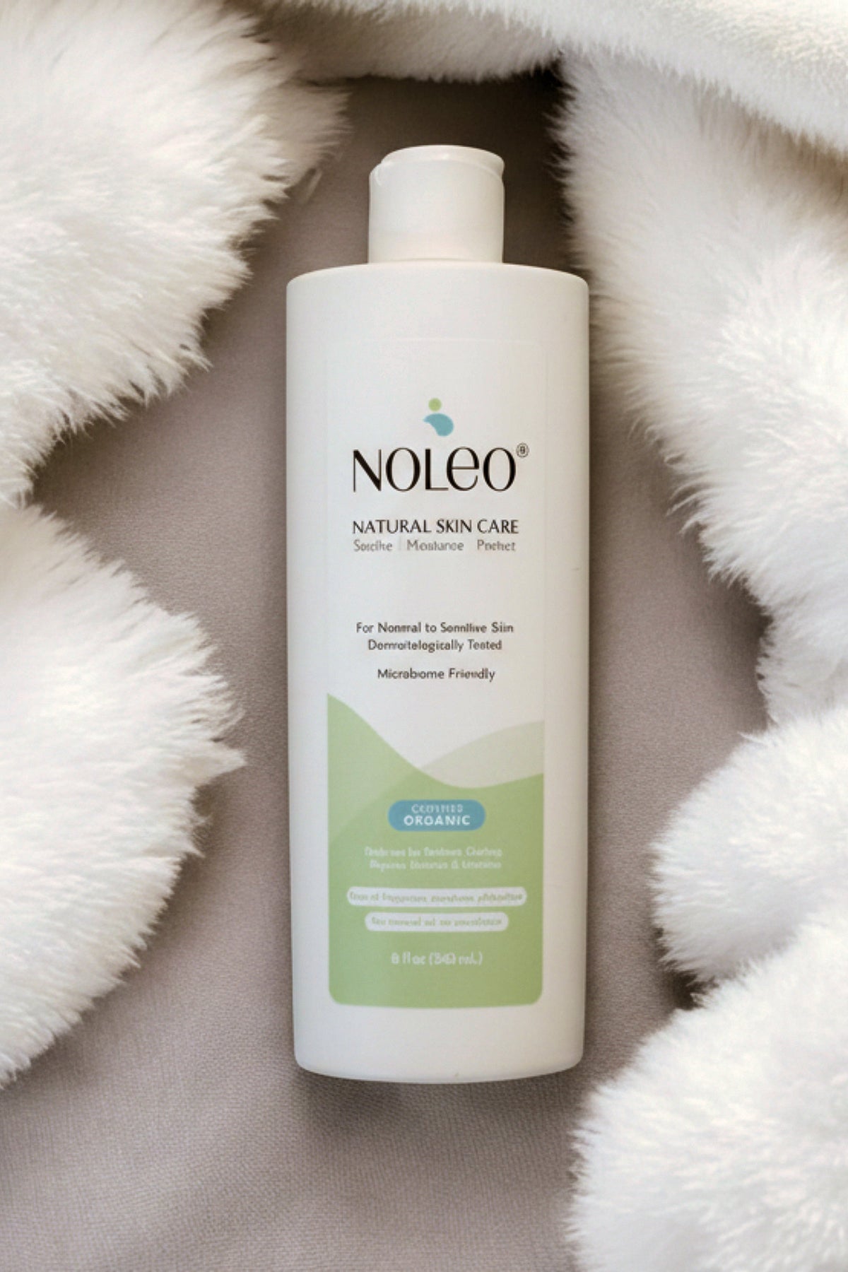 A white bottle of NOLEO Natural Skin Care deep moisturizer is displayed on a soft, light-colored fabric surface.