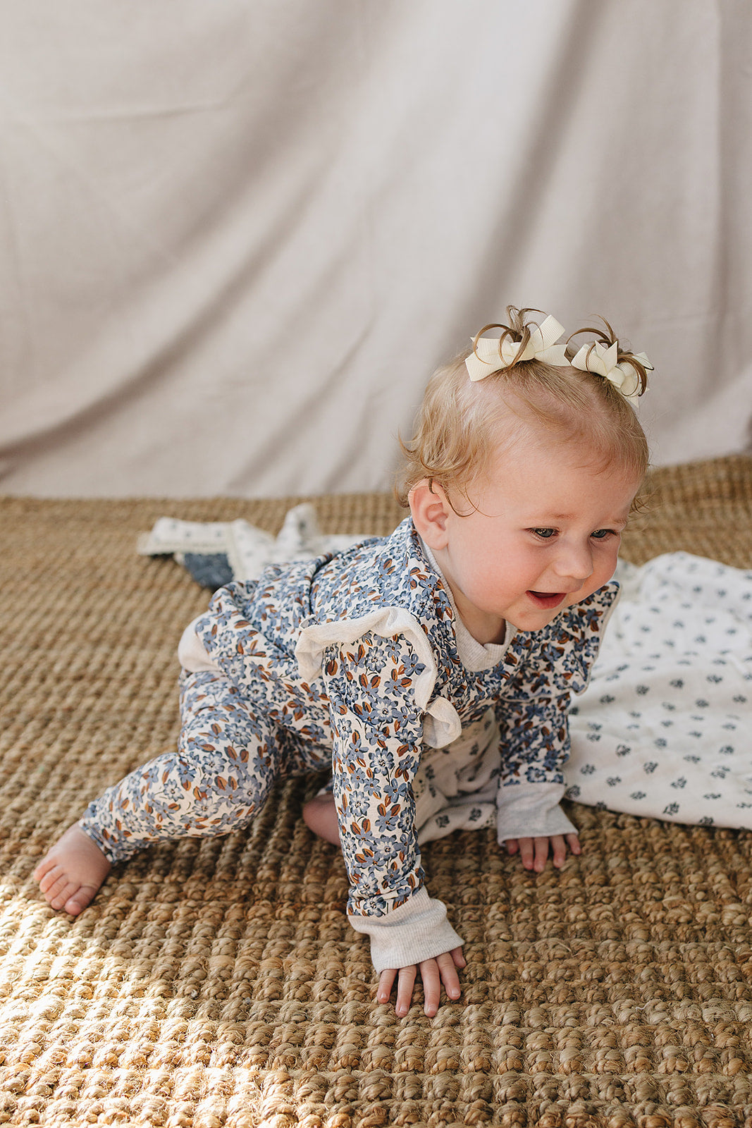A baby girl crawls on a woven rug, wearing a floral-patterned long sleeve cotton set with ruffle details. Soft, breathable fabric ensures comfort for everyday adventures and play.