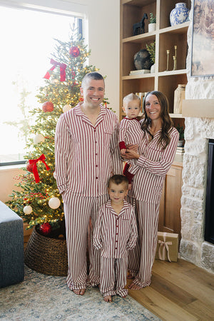 A family in matching red striped bamboo pajama sets stands by a decorated Christmas tree, showcasing a cozy holiday atmosphere.