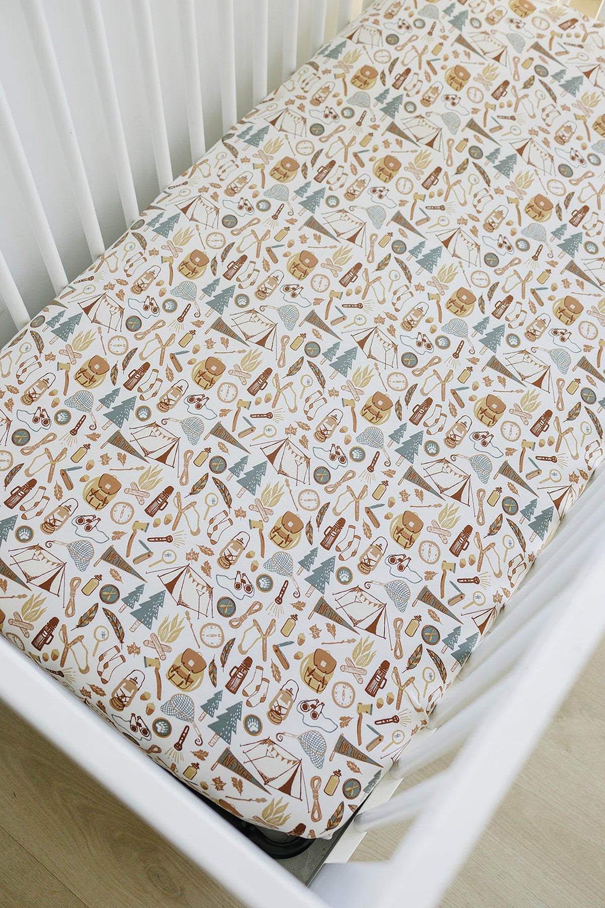 Crib sheet with a camping-themed pattern featuring tents, trees, and camping gear on a white background.