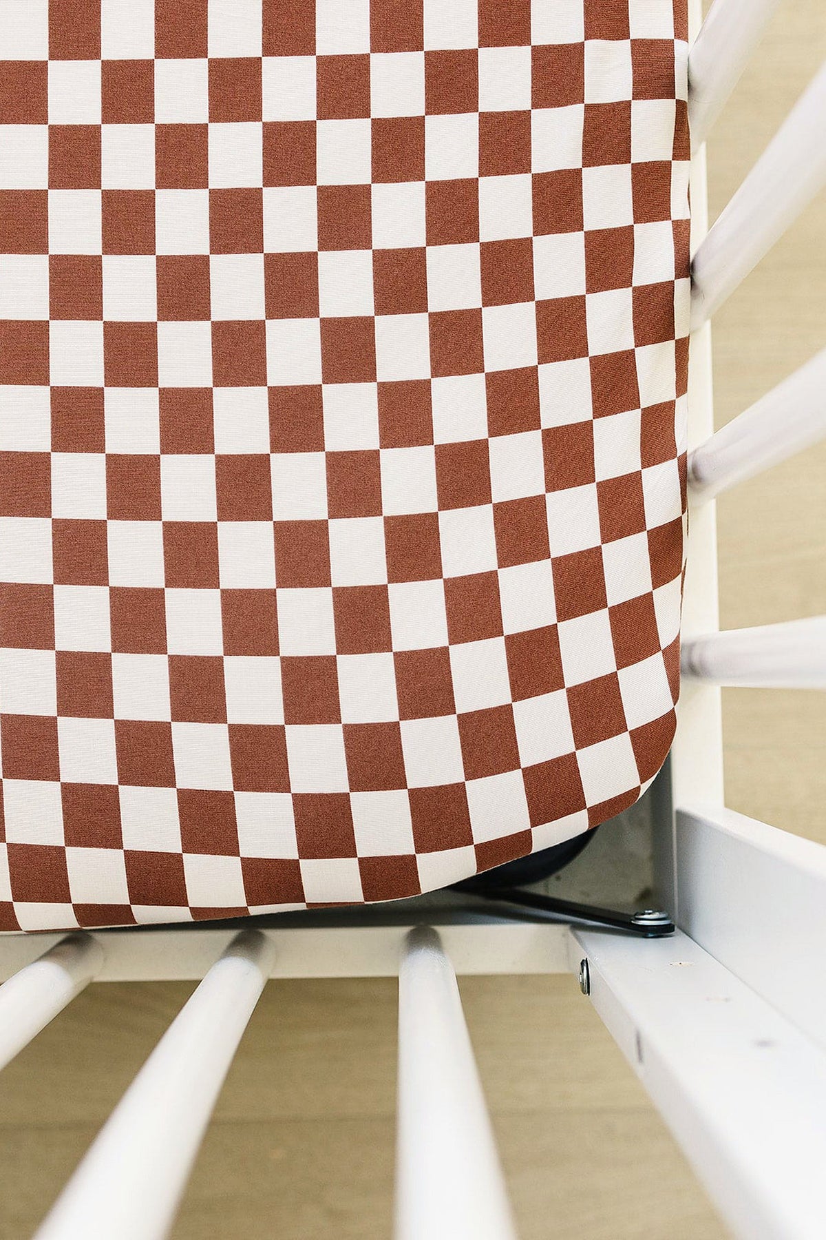 Rust and white checkered crib sheet made from soft bamboo fabric, fitted on a white crib.