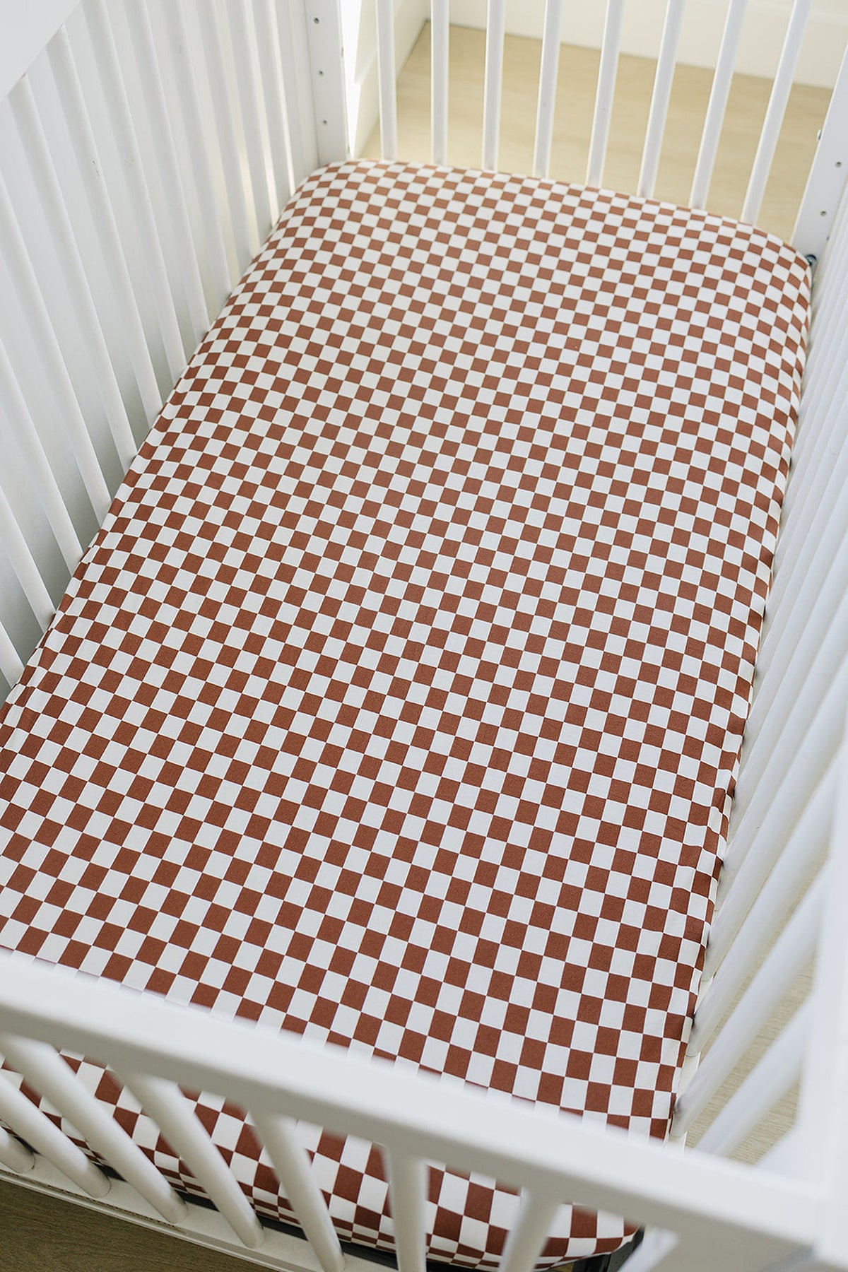 White crib with a rust checkered bamboo crib sheet, showcasing a stylish and cozy nursery setting.