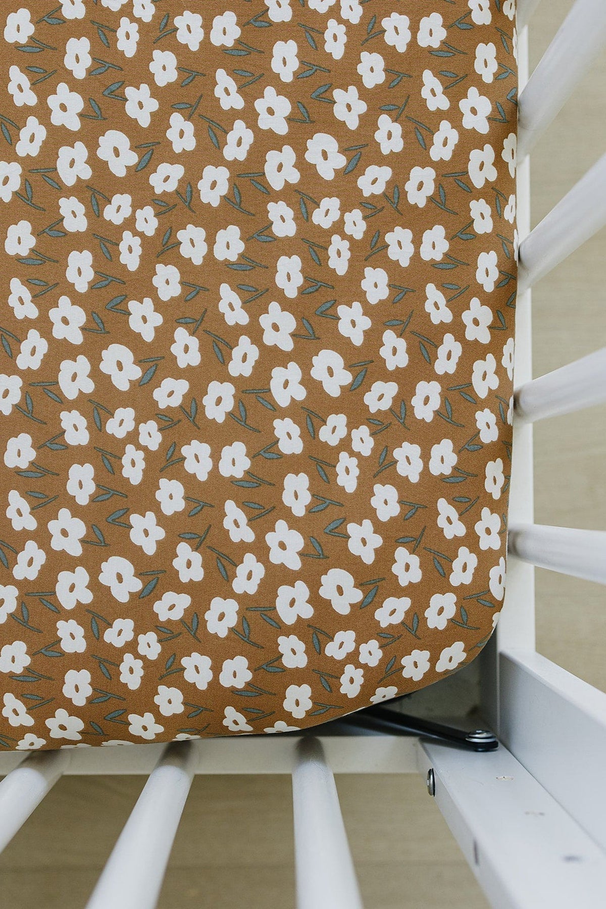 White crib with a mustard floral bamboo crib sheet featuring white flowers and green leaves, providing a stylish look.