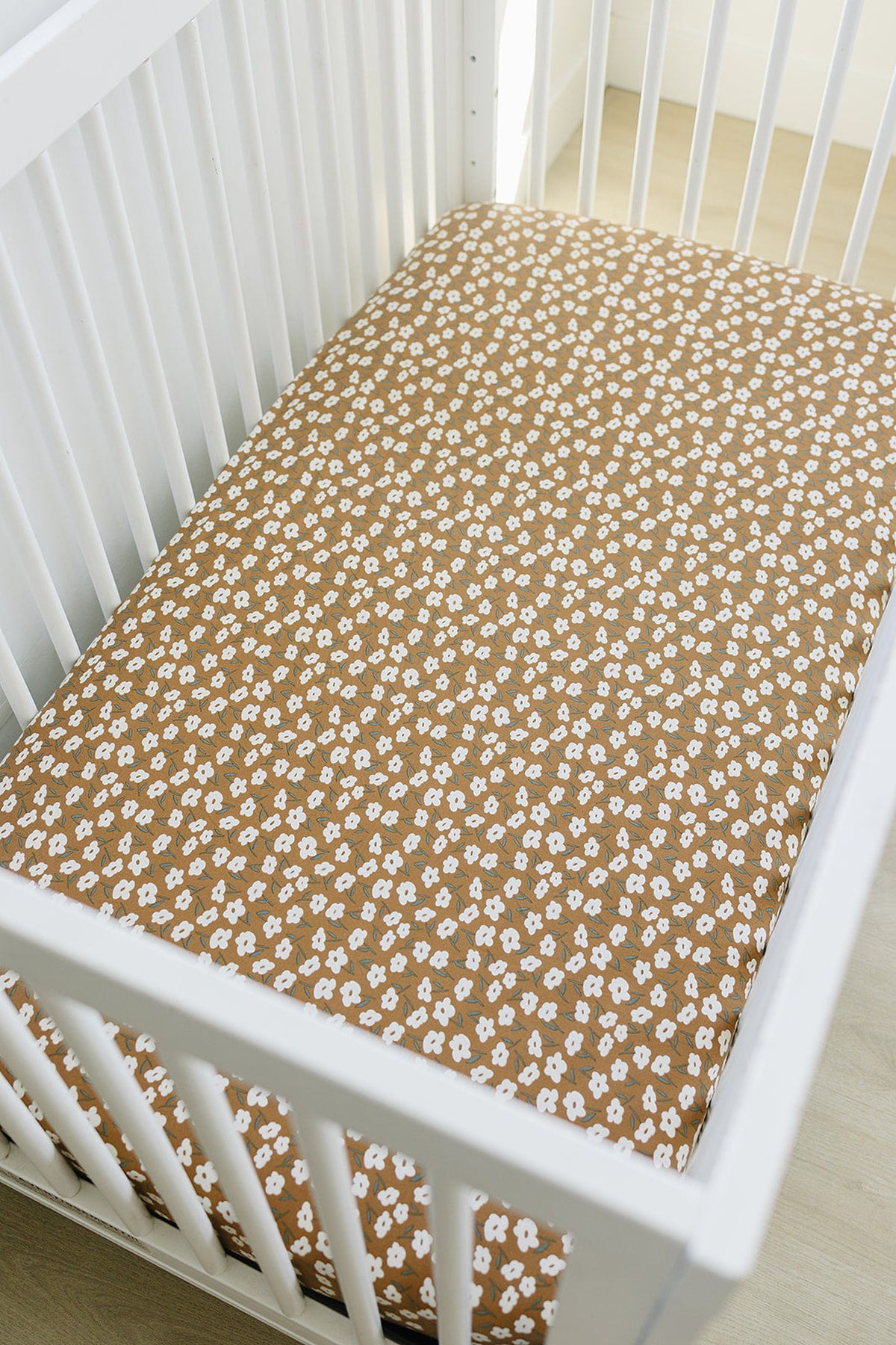 A white crib with a mustard floral stretch crib sheet made of bamboo fabric, showcasing a cozy nursery setting.