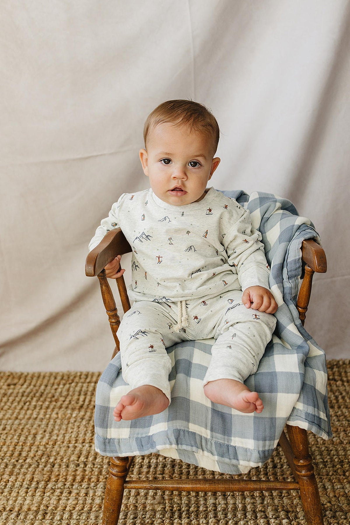 A young child sits in a wooden chair, wearing a light beige French terry cotton set adorned with playful skier patterns.