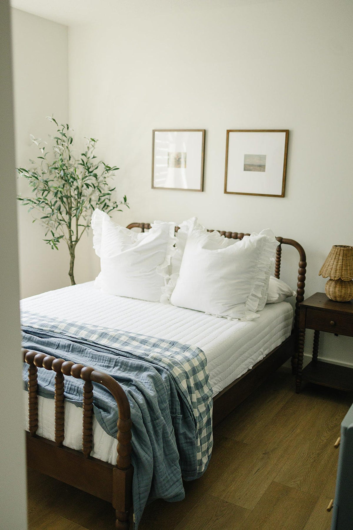 A cozy bedroom with a wooden bed features a white quilt, white pillows, and a blue gingham blanket.