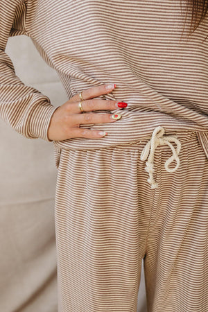 A close-up of a person wearing a beige striped cotton loungewear set, featuring a relaxed fit and drawstring waist. The outfit emphasizes comfort and style for casual wear.