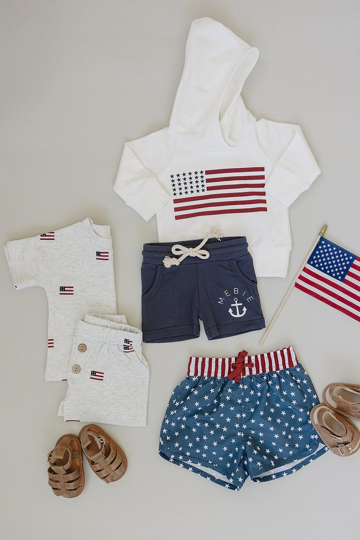 Baby clothing set includes a white hoodie with an American flag, navy shorts, and star-patterned swim trunks.