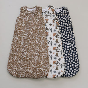 Three beautifully designed baby sleep sacks are displayed, featuring a brown floral pattern, a white print with cacti and animals, and a navy floral design, all made from soft, breathable.