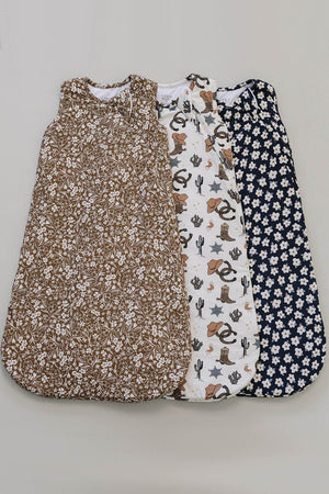 Three baby sleep sacks are displayed, featuring various prints: a brown floral design, a white pattern with cowboy motifs, and a navy sack adorned with daisies.