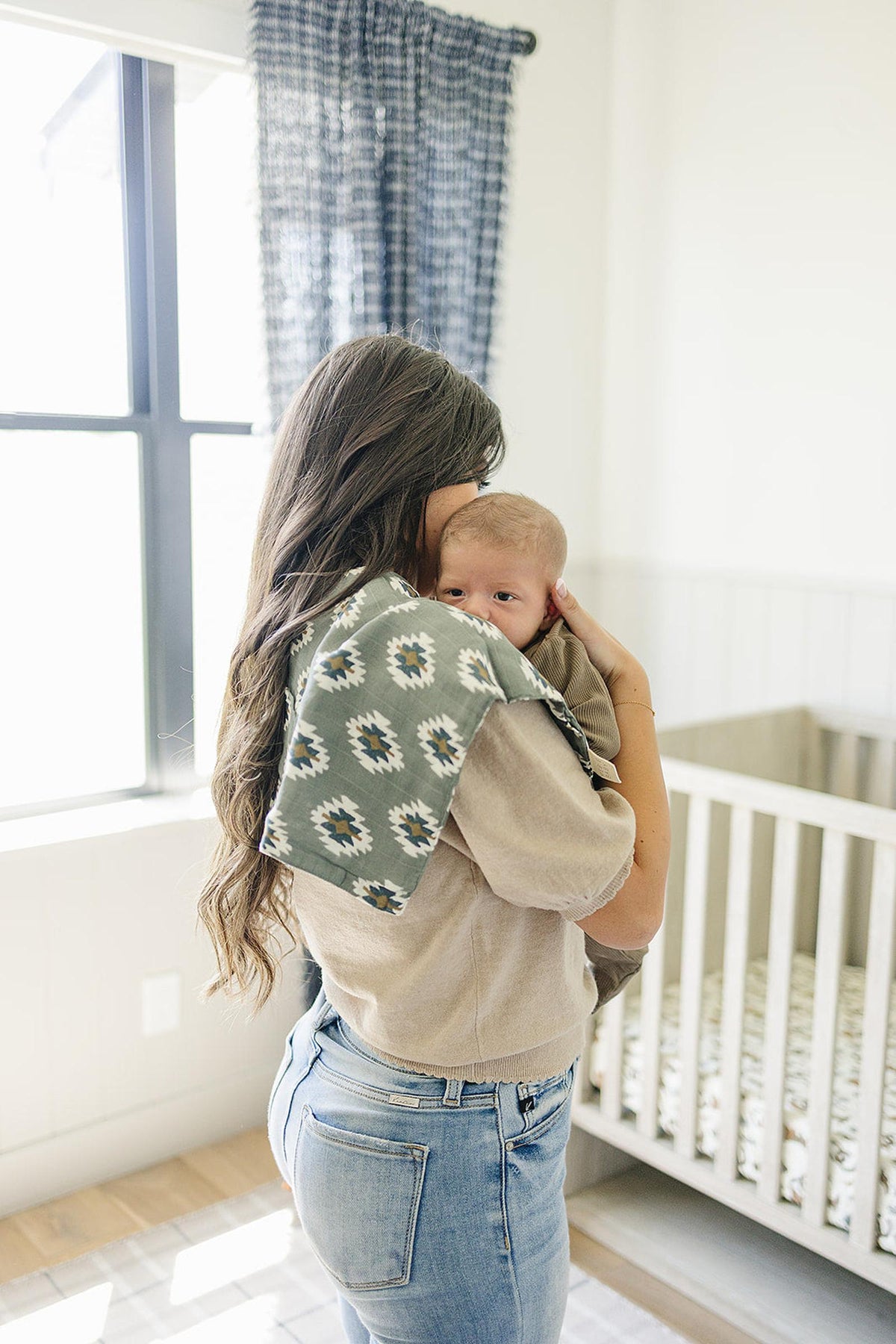 A woman holds a baby with a Southwest Aztec muslin burp cloth on her shoulder in a nursery.