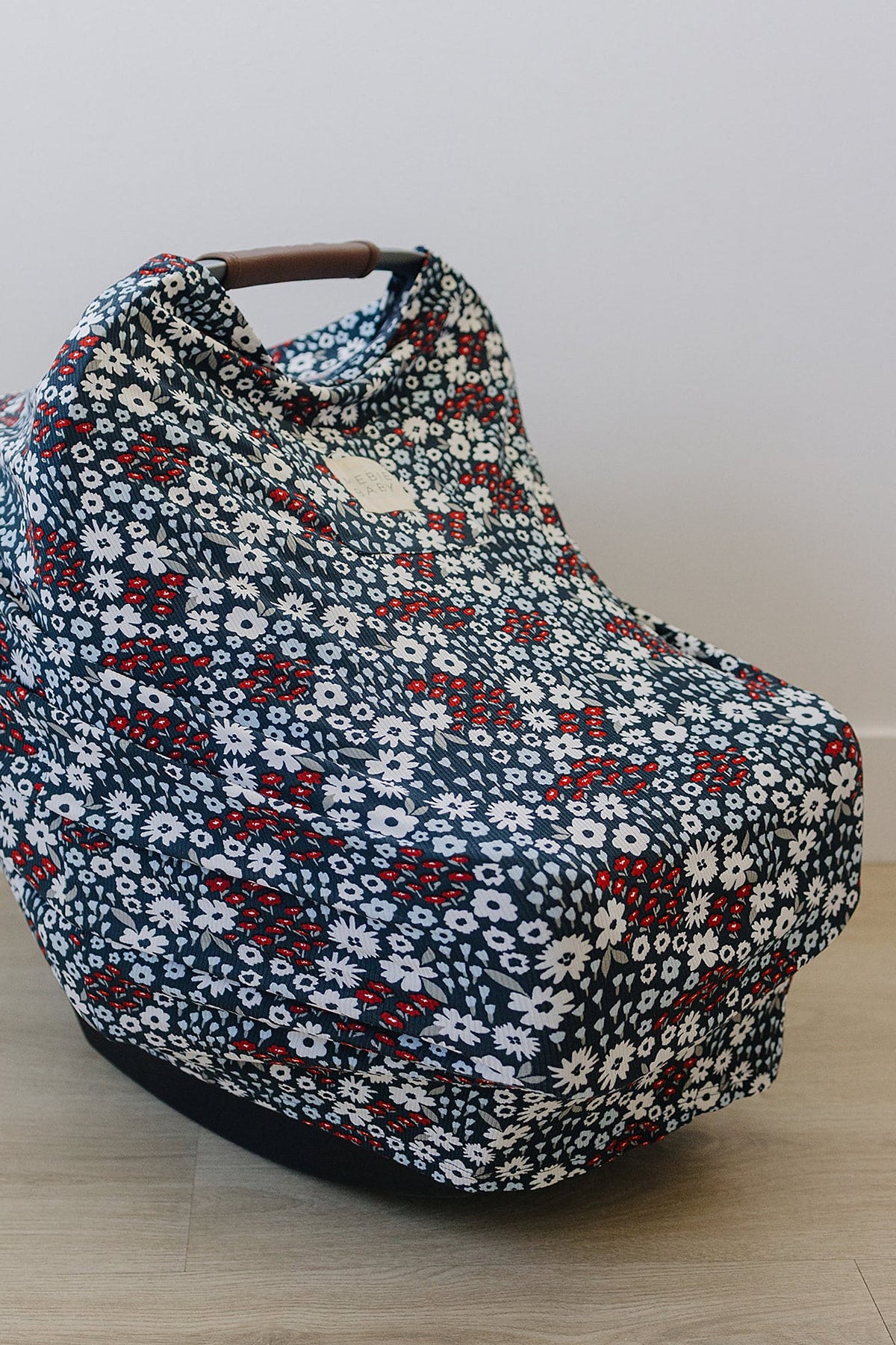 Floral-patterned car seat cover with red, white, and blue flowers on a wooden floor. Made from bamboo fabric.