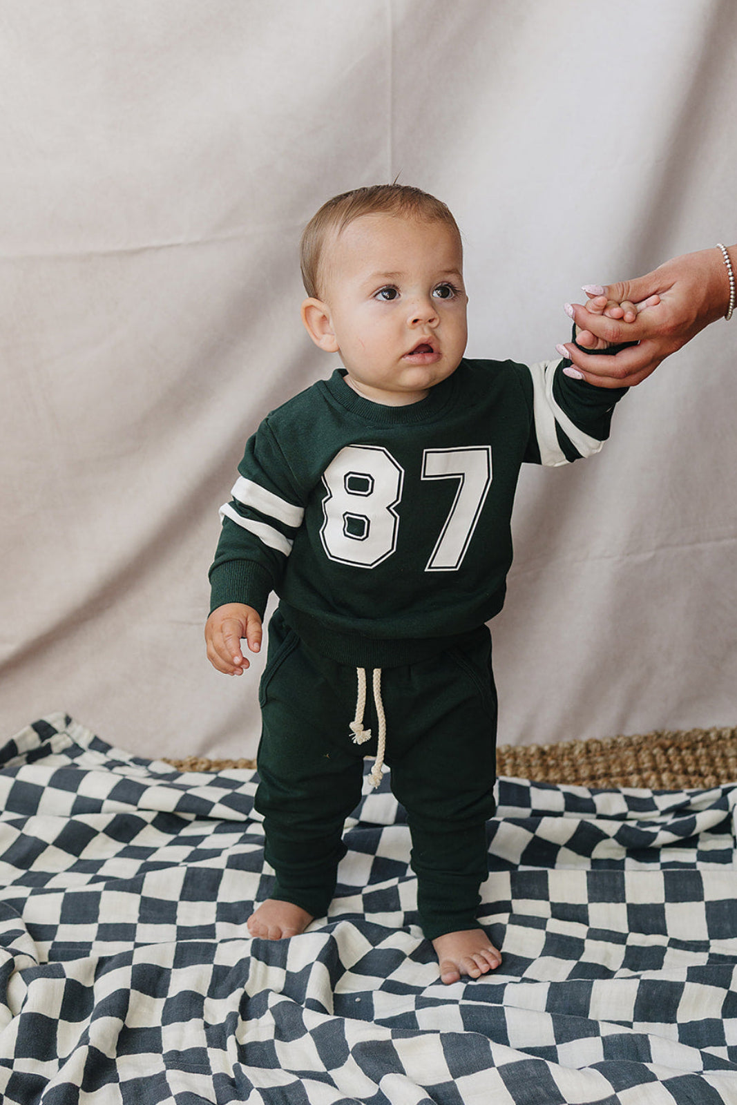 A baby wearing a dark green French terry cotton set features a sporty design with the number 87 on the shirt.