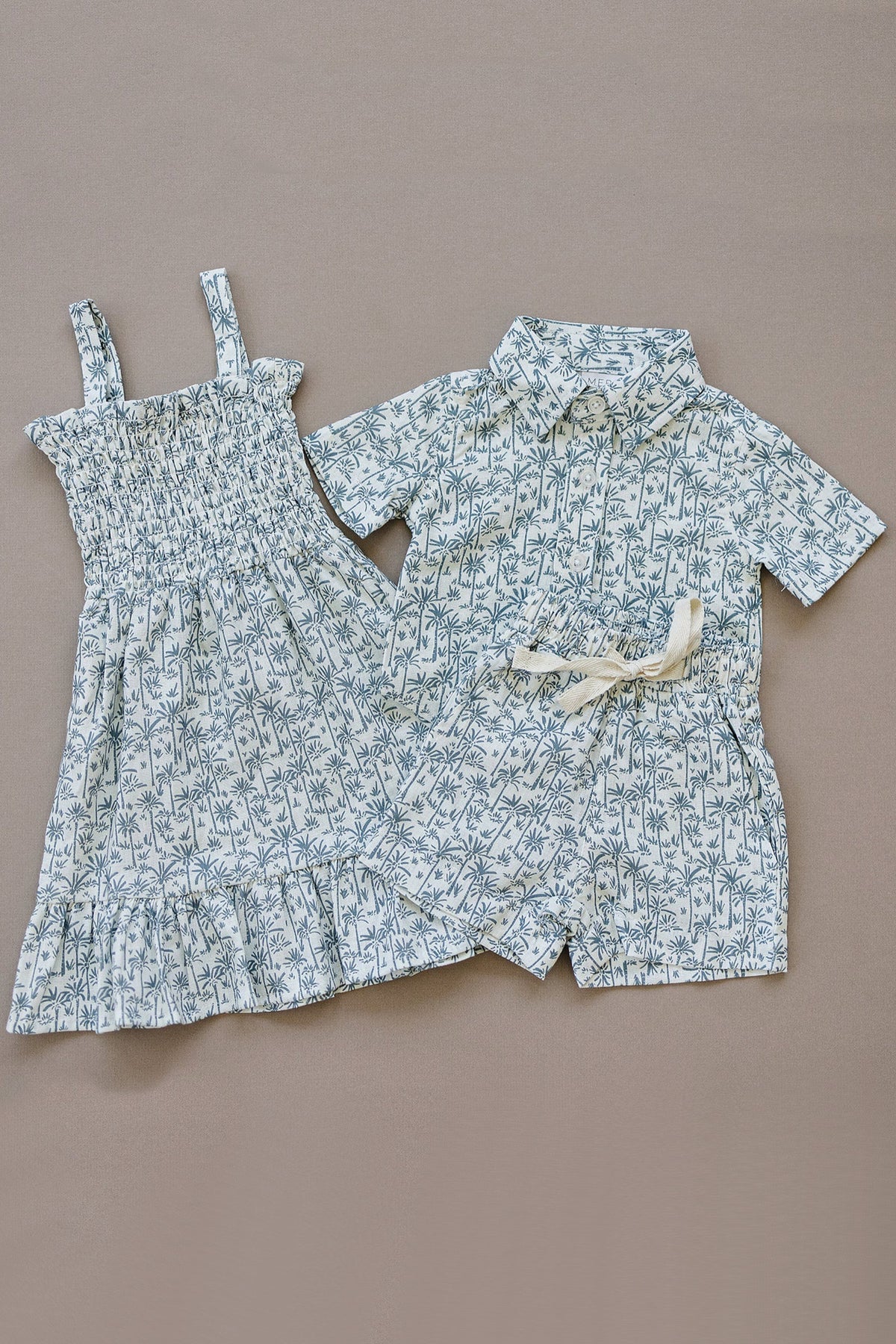 Two childrens outfits with a palm tree pattern, featuring a dress and a button-up shirt with shorts.