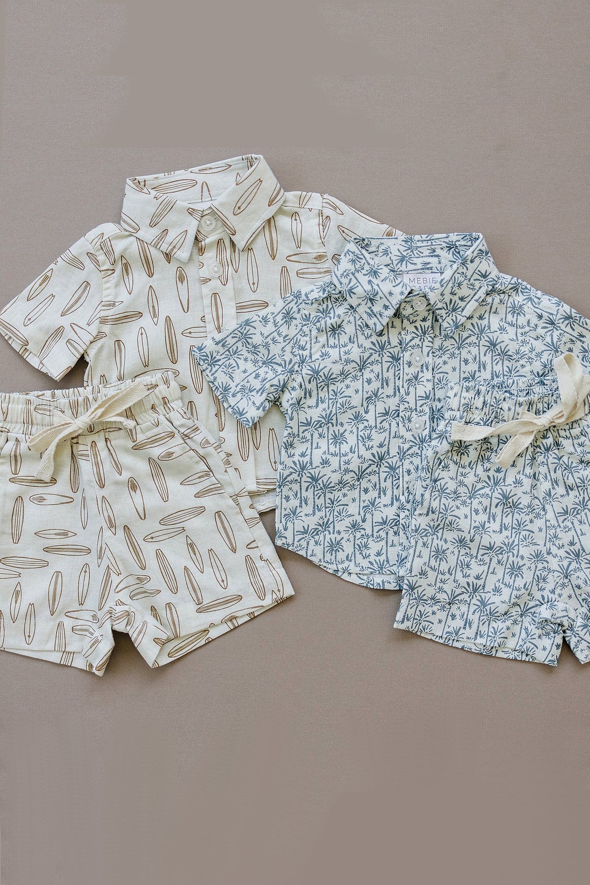 Two linen button-up shirts with surfboard and palm tree patterns, paired with matching shorts, on a neutral background.