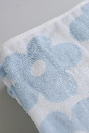 Light blue and white beach towel featuring a floral pattern, made from 100% organic cotton. Soft and absorbent, it is ideal for eco-friendly beach outings and family use.