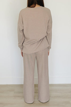 A woman is seen from behind, wearing a beige striped loungewear set made of soft cotton. The outfit features a relaxed fit, perfect for comfortable lounging at home.