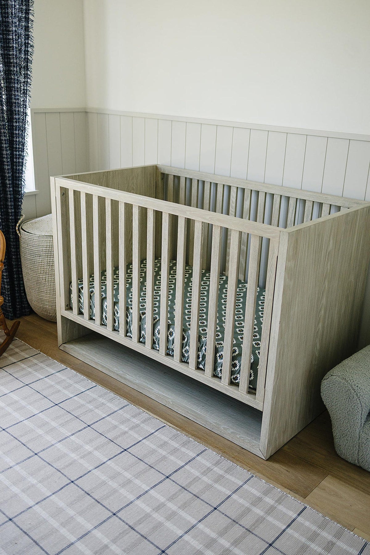 Wooden crib with a Southwest Aztec patterned muslin sheet, set in a cozy nursery with neutral decor.