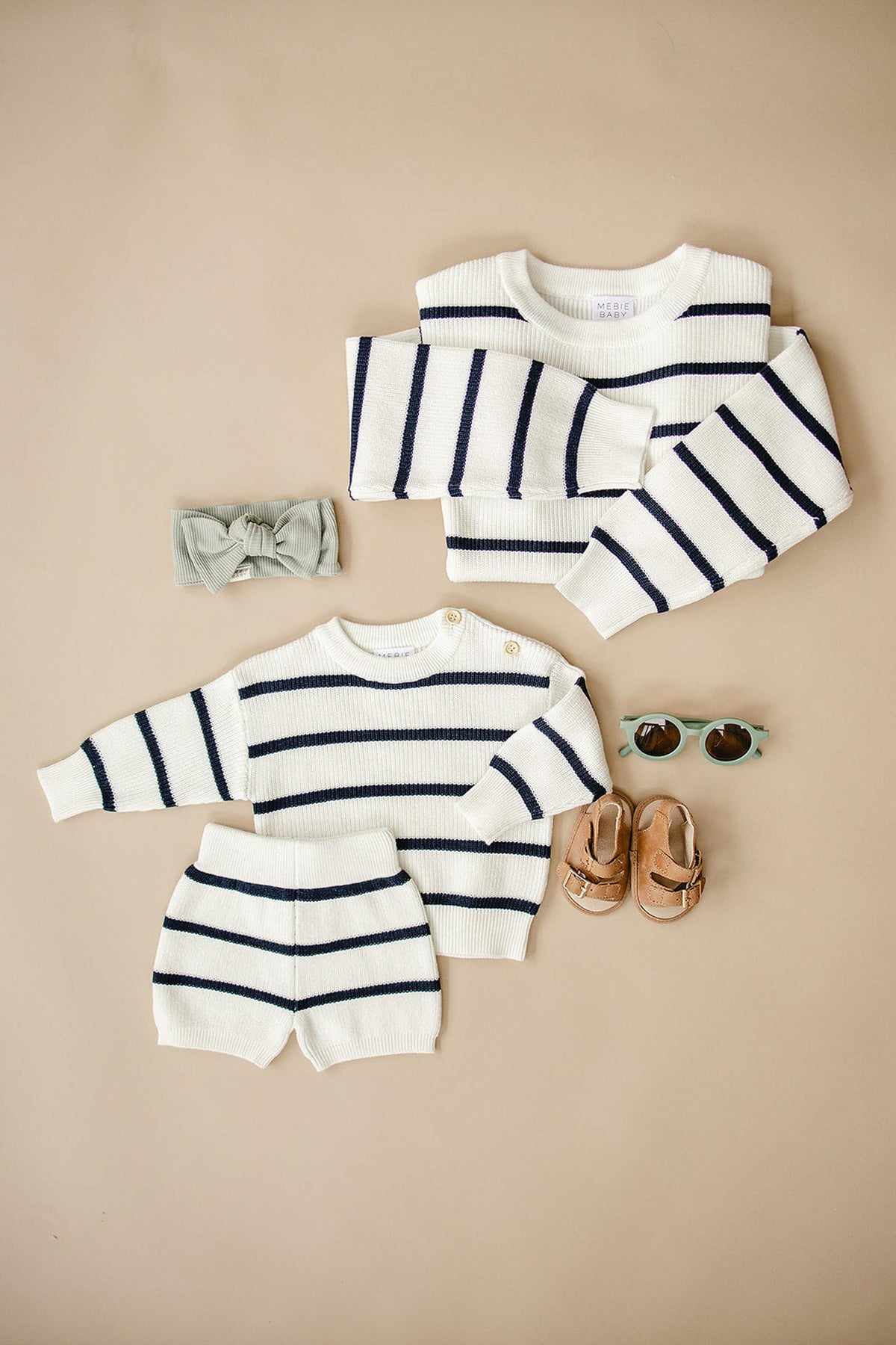 White and navy striped childrens knit sweater and shorts set, with a headband, sunglasses, and sandals nearby.