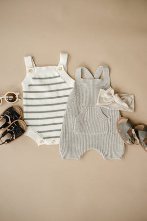 Gray knit overalls and striped romper with sandals, sunglasses, and a headband on a beige background.