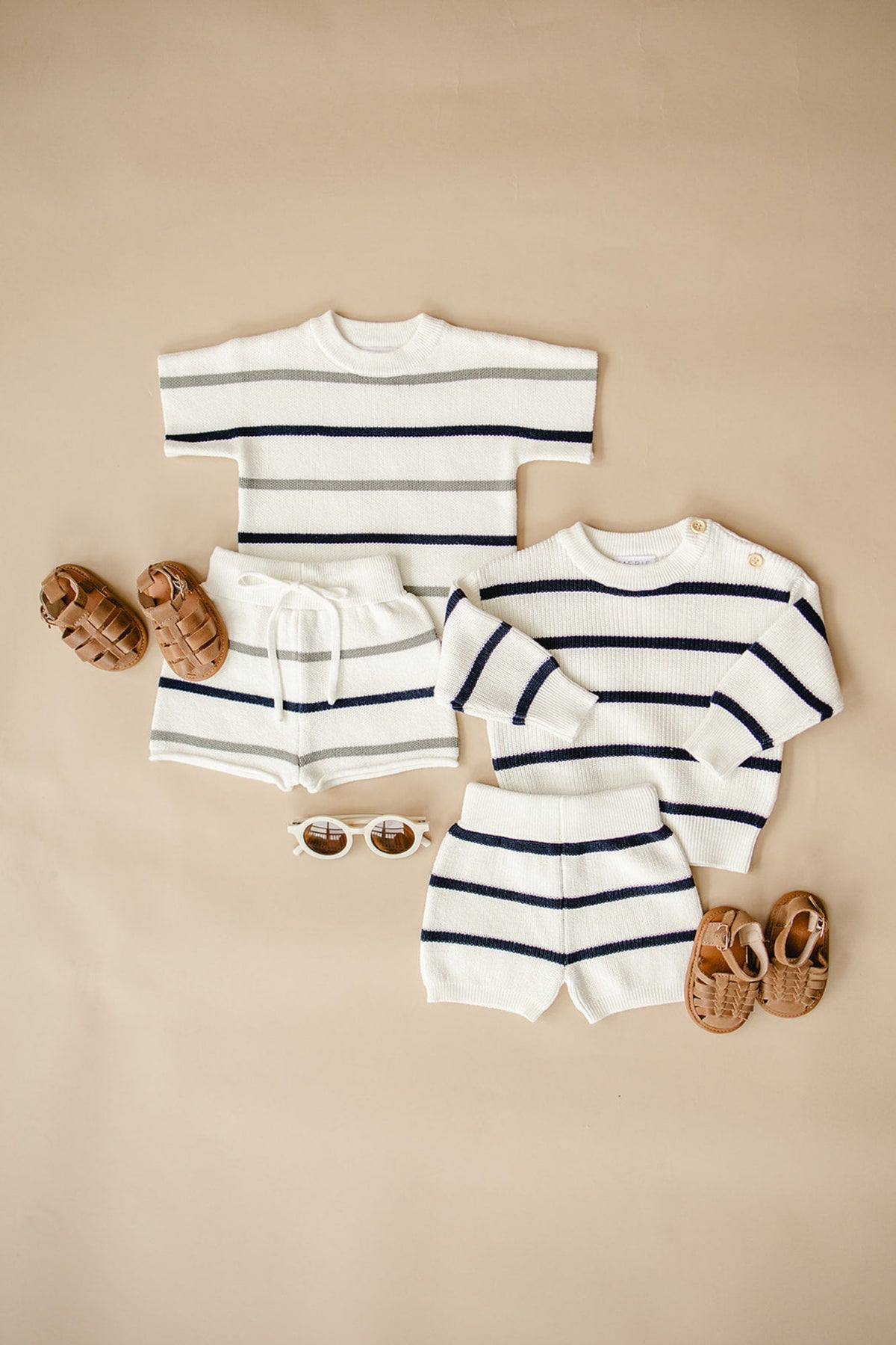 Striped knit baby outfits in white, sage, and navy with matching shorts, sandals, and sunglasses on a beige background.