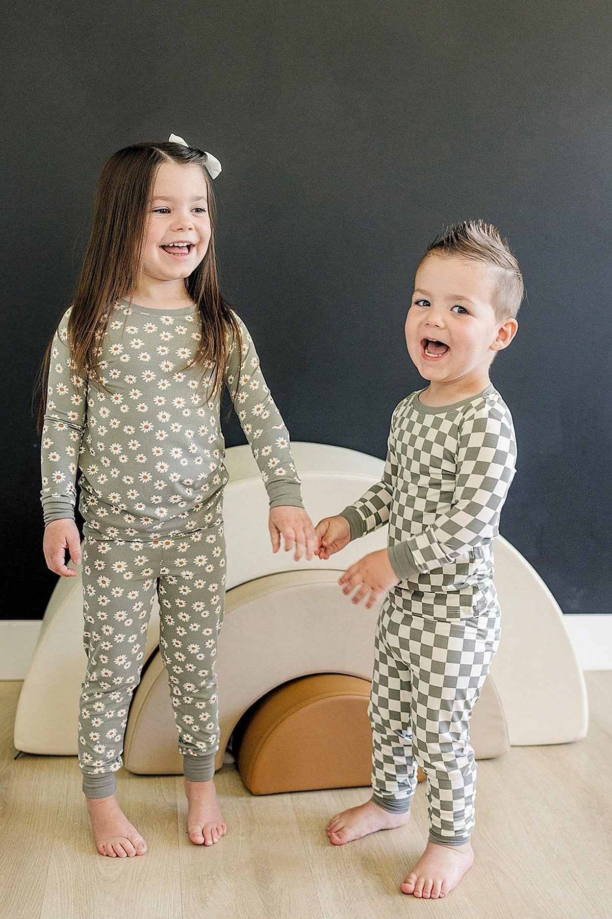 Two children in cozy pajamas; one in a floral pattern, the other in light green checkered.