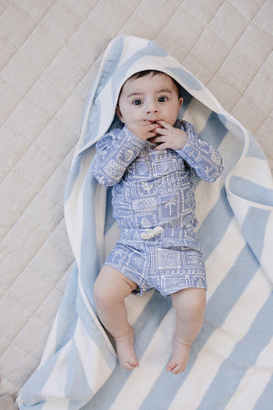 A baby lies on a soft, beige blanket, wrapped in a light blue and white striped hooded towel.