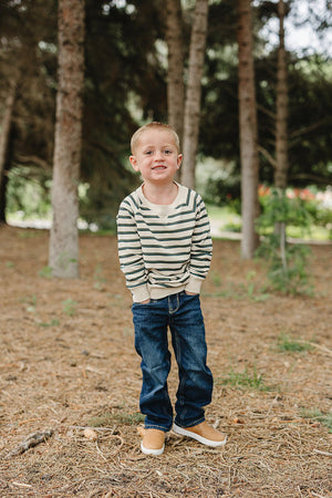 A young child stands in a wooded area, wearing a soft, striped long-sleeve crewneck shirt and blue jeans. The shirt features a relaxed fit, perfect for playtime or casual outings.