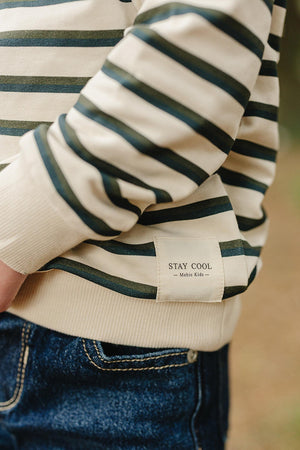 A close-up of a childs striped long-sleeve t-shirt featuring green and beige stripes. The shirts label reads STAY COOL from Mebie Kids, made from soft, breathable cotton.
