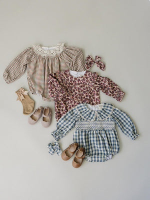 Three baby girl outfits are displayed on a light gray background, featuring a camel gingham romper, a floral print dress, and a blue gingham romper, paired with matching accessories and.