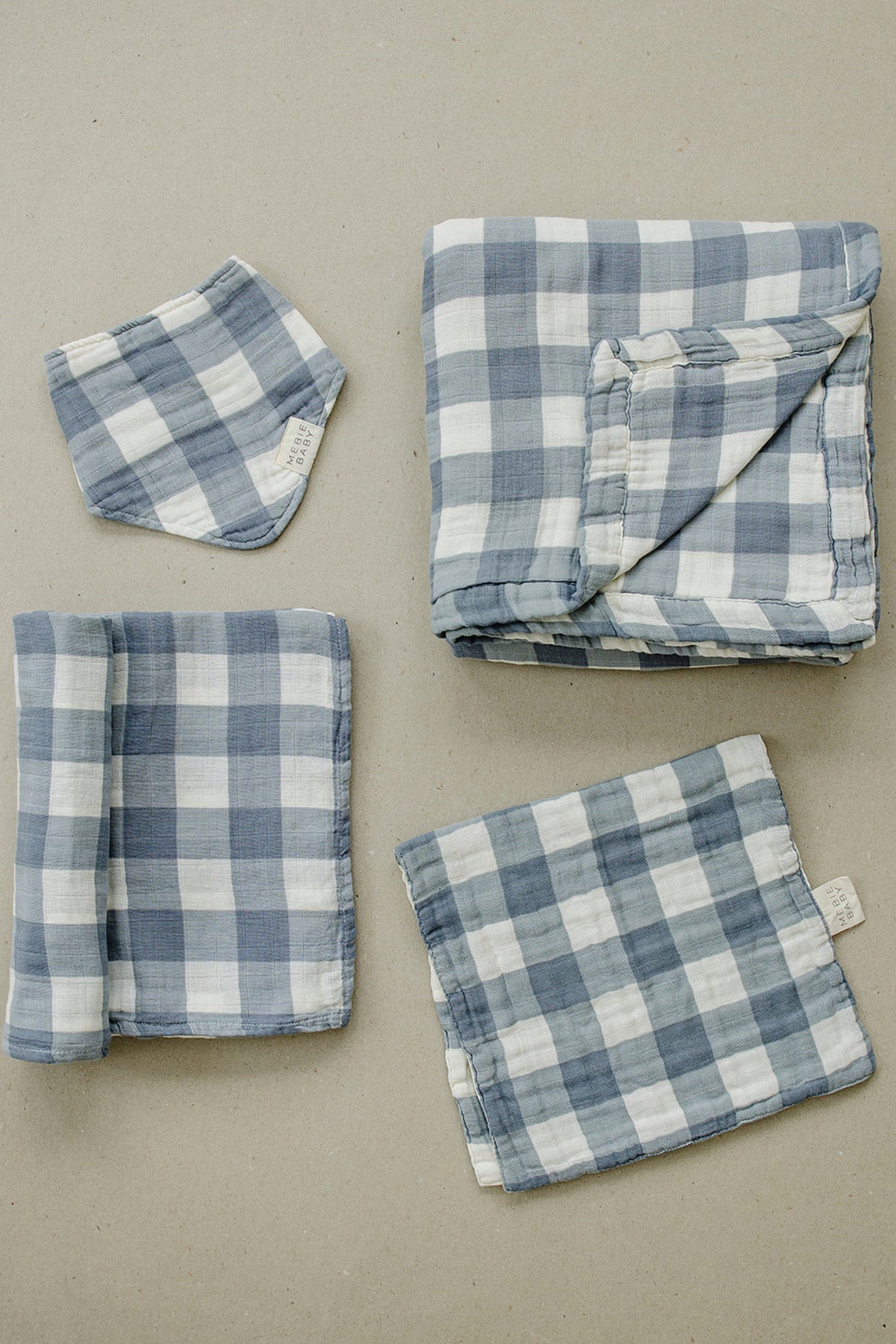 Dusty blue gingham muslin cloths, including a burp cloth and quilt, displayed on a neutral background.