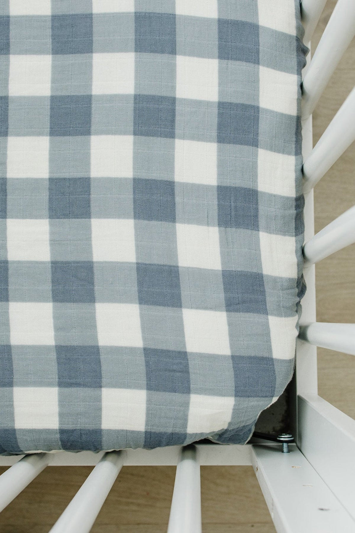 Dusty blue gingham muslin crib sheet on a white crib, showcasing a soft cotton texture and classic pattern.