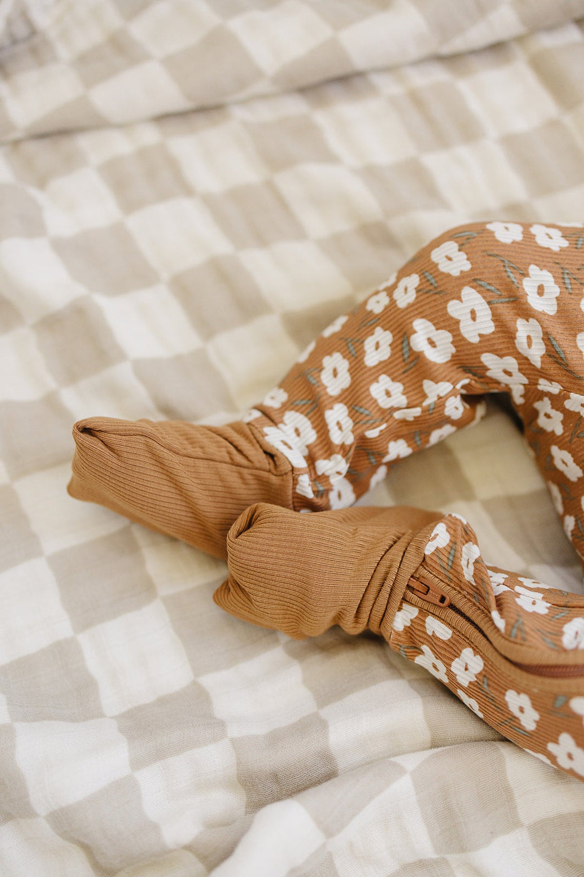 Baby wearing mustard floral ribbed pajamas with a zipper, lying on a beige and white checkered blanket.